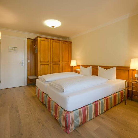 A covered double bed stands in the middle of the hotel room, next to it is a large wardrobe