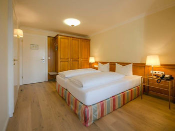 Ein bezogenes Doppelbett steht in der Mitte des Hotelzimmers, daneben ist ein großer Kleiderschrank