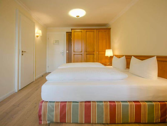 Ein bezogenes Doppelbett steht in der Mitte des Hotelzimmers, daneben ist ein großer Kleiderschrank