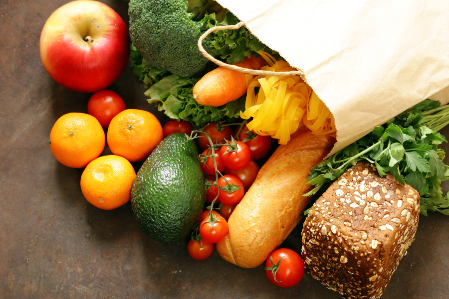 Lebensmittel aus einer Papiertüte: frisches Obst, Gemüse, Brot und Pasta.