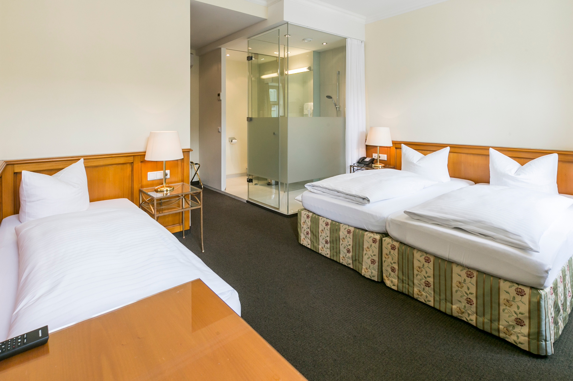 Camera luminosa con tre letti, eleganti accenti in legno e bagno moderno.