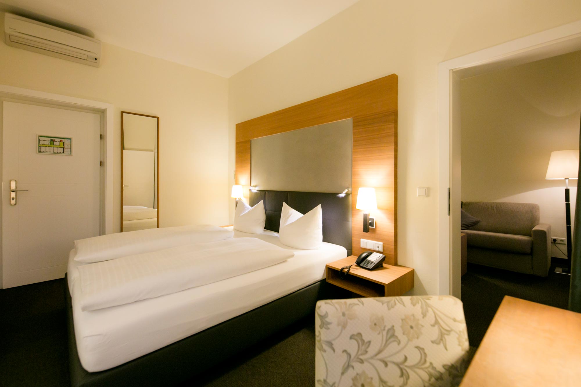 Gemütliches Doppelzimmer mit warmen Holzakzenten und weichen, weißen Bettdecken.