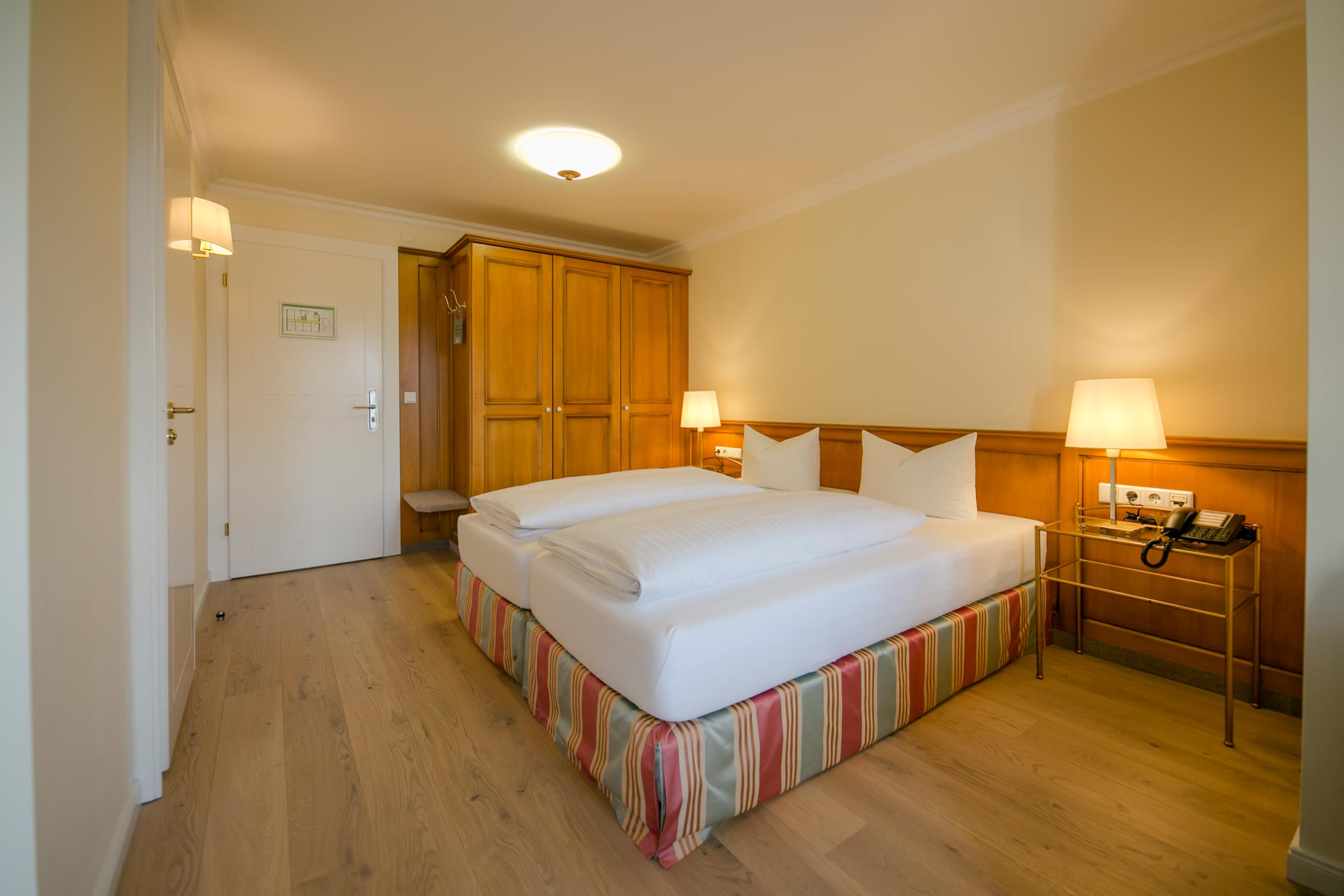 Gemütliches Zimmer mit Holzmöbeln, weicher Beleuchtung und Doppelbett mit weißen Kissen.