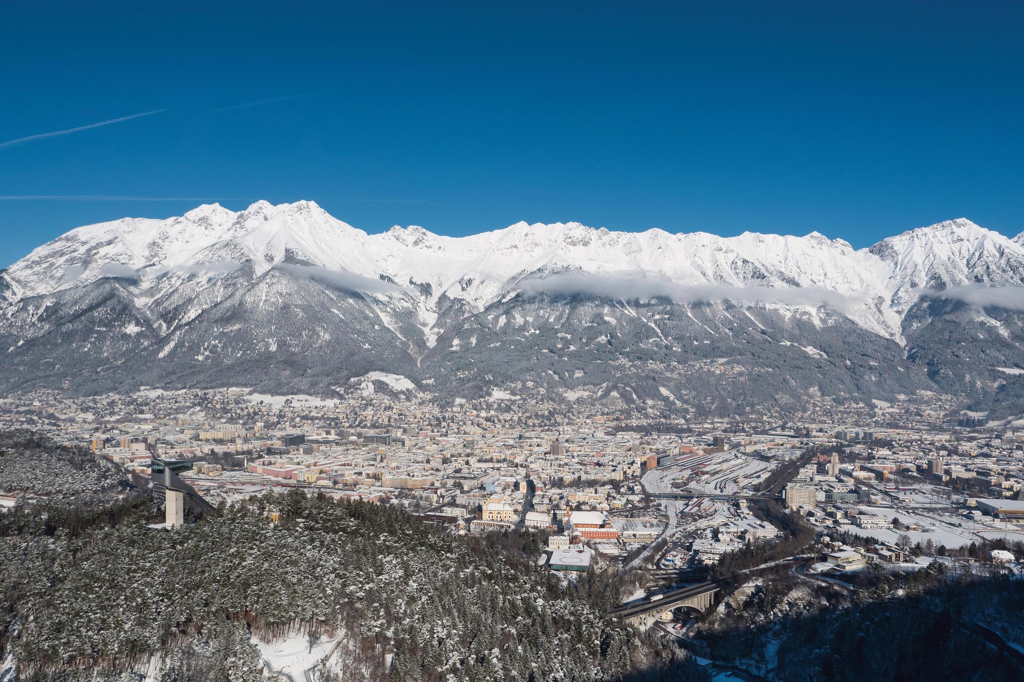 Snow-covered mountains and Innsbruck under a bright blue sky in winter.