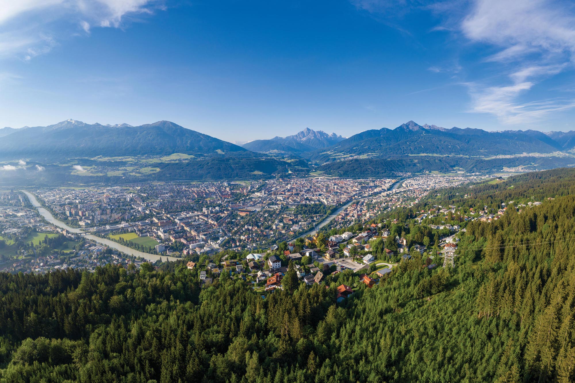 Vista mozzafiato sulla città, sul fiume e sulle montagne sotto un cielo azzurro e limpido.