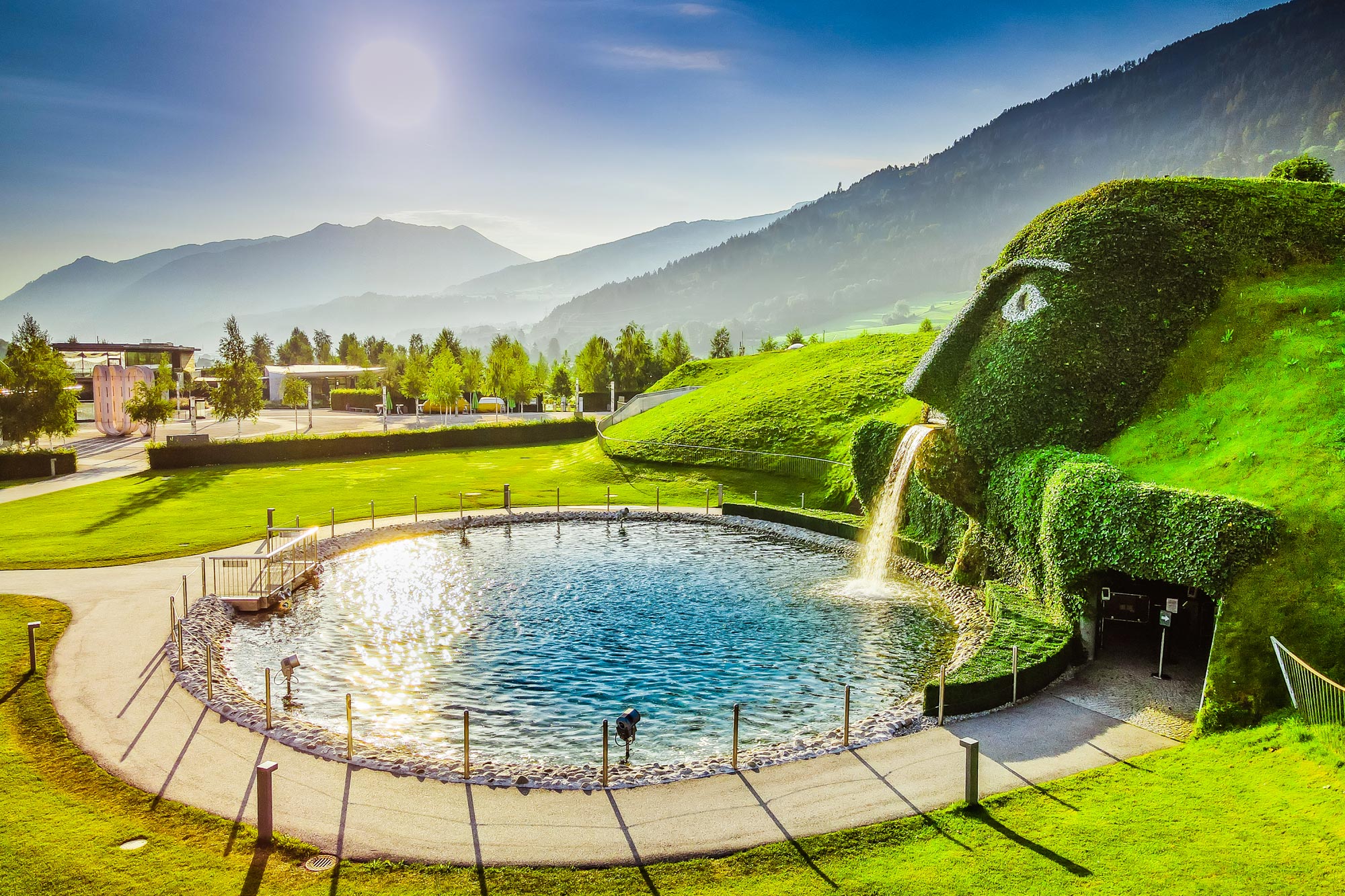 Gigante verde con cascata e pittoresco sfondo montano sotto il sole.