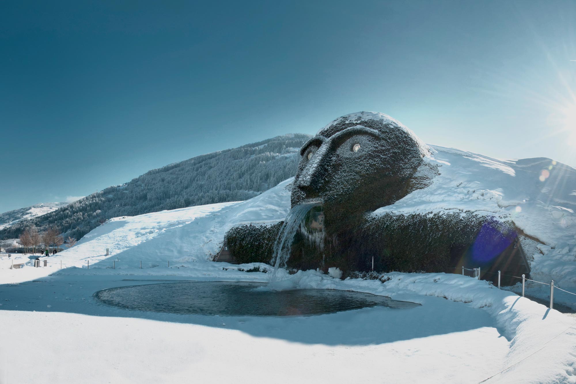 Paesaggio innevato con impressionante scultura della testa e cascata sotto il sole.
