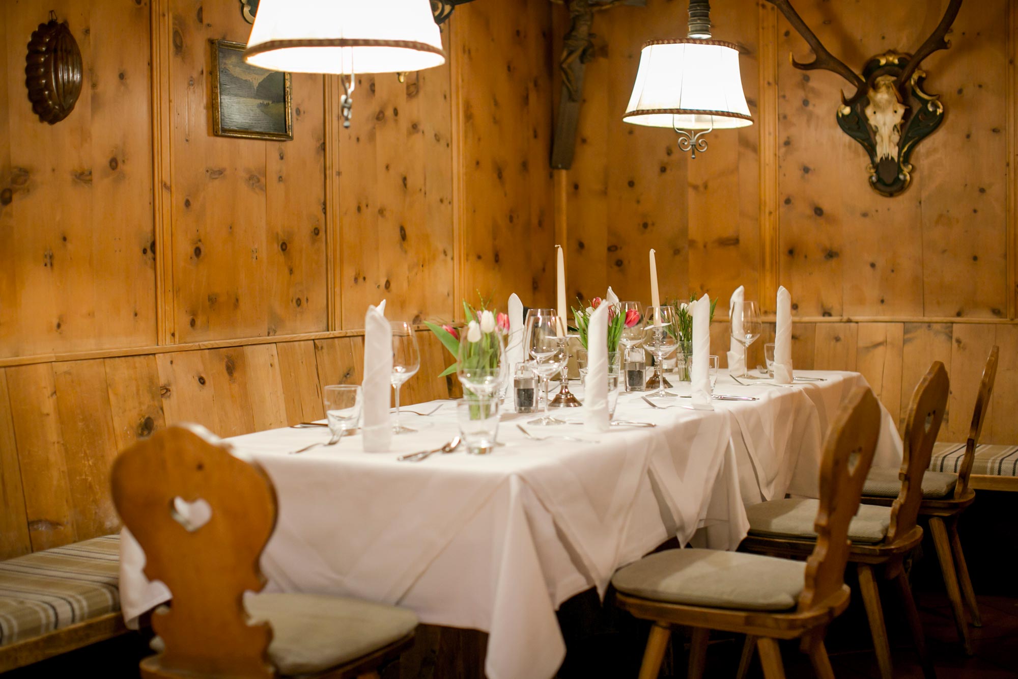 Long dining table with white tablecloths and wooden chairs in a cozy room.