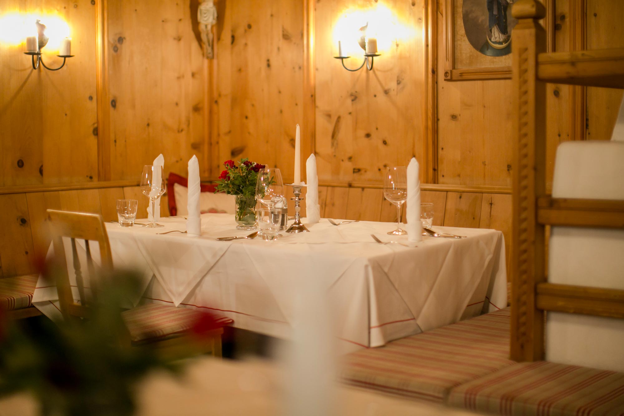 Holzwand mit Kerzenlicht, gedeckter Tisch, gemütliche Atmosphäre, warme Beleuchtung, rote Blumen.