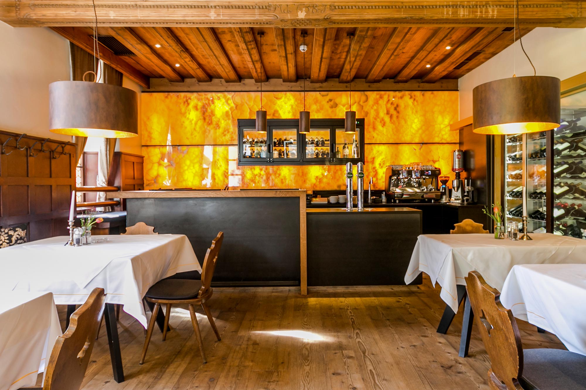 Restaurant mit gemütlicher Holzdecke und beleuchteter Onyx-Wand hinter der Bar.