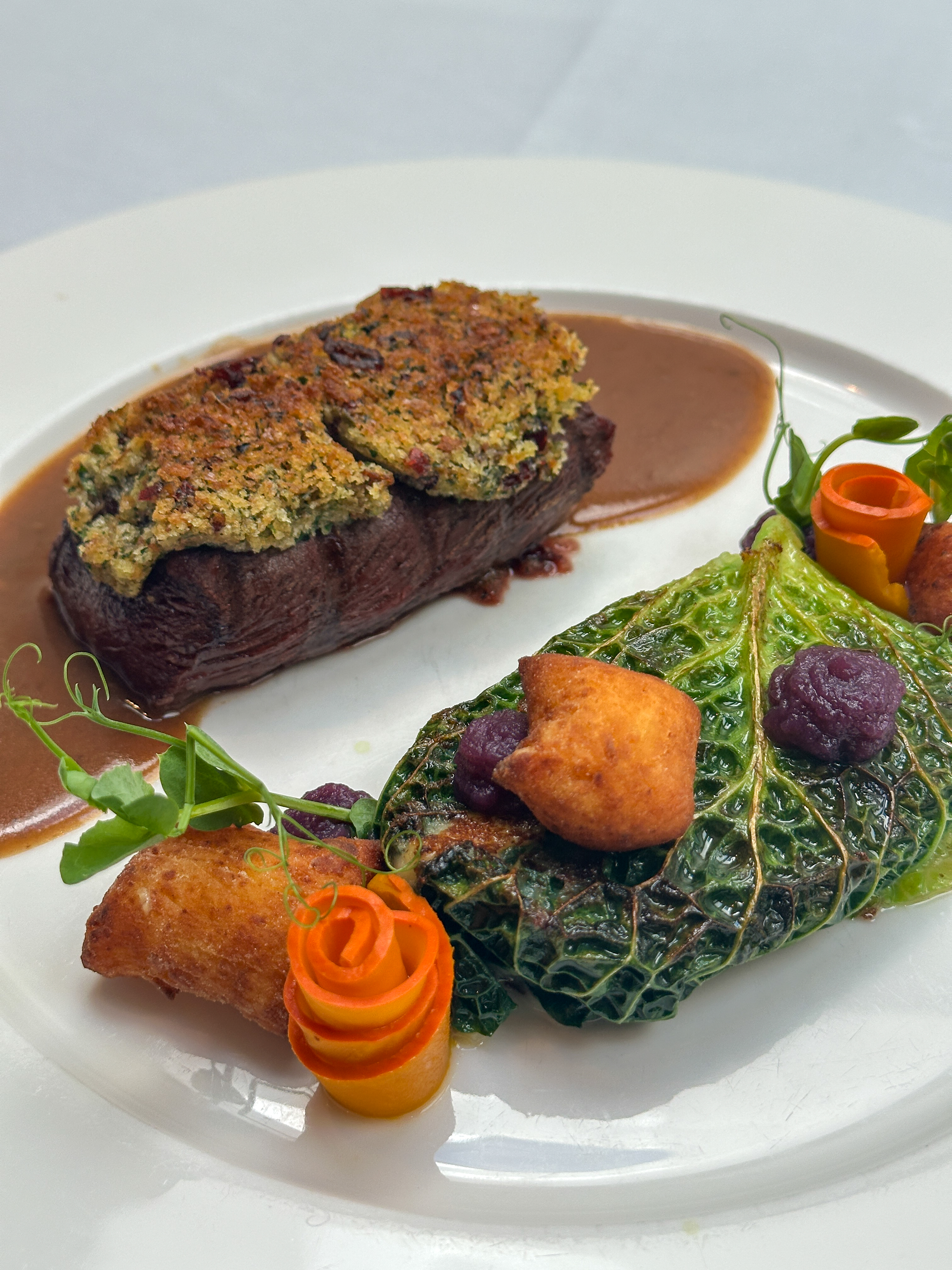 Elegant meat dish with crust, vegetables and sauce served on a white plate.