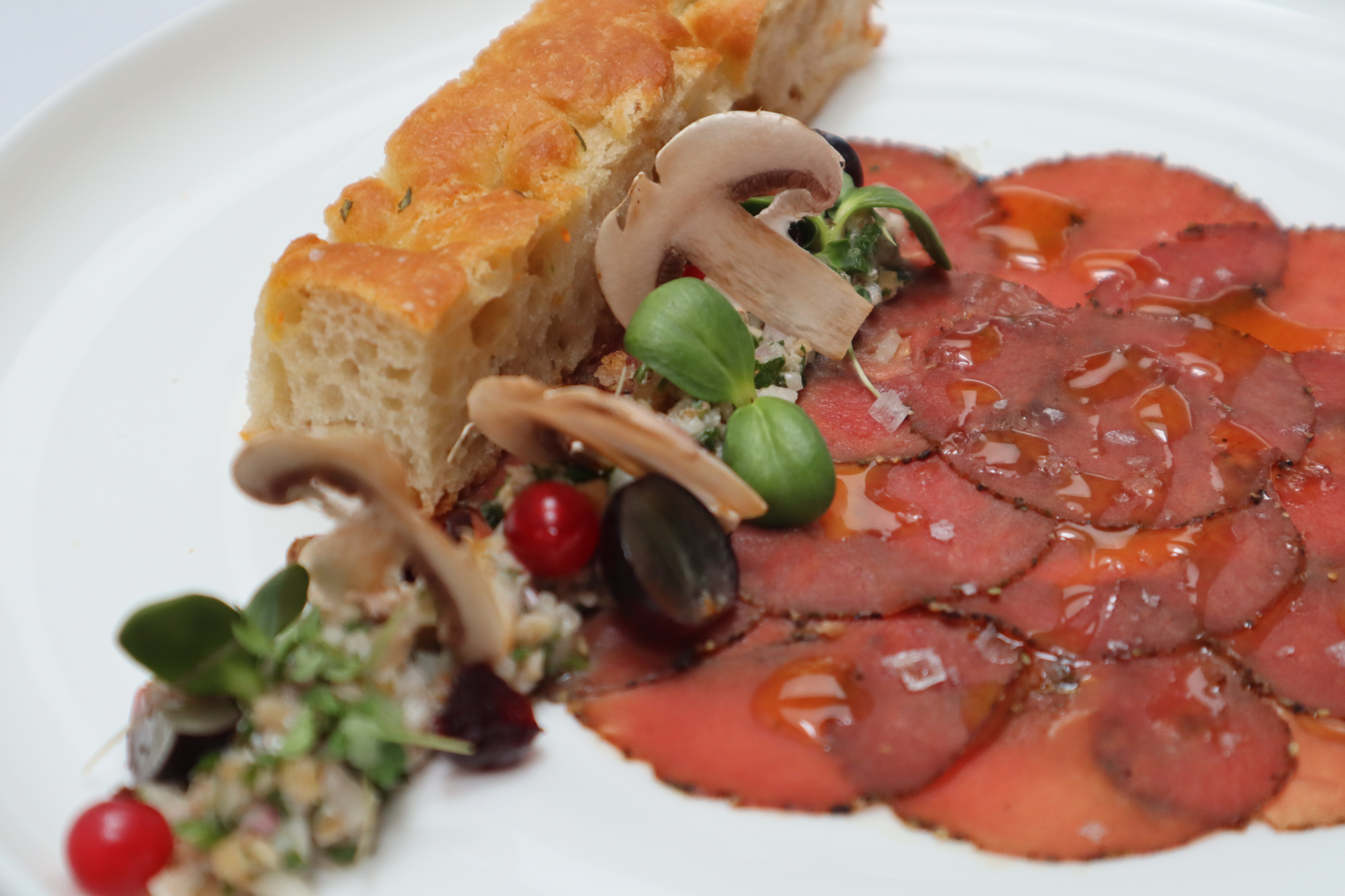 Carpaccio with fresh mushrooms and crusty bread served on a white plate.